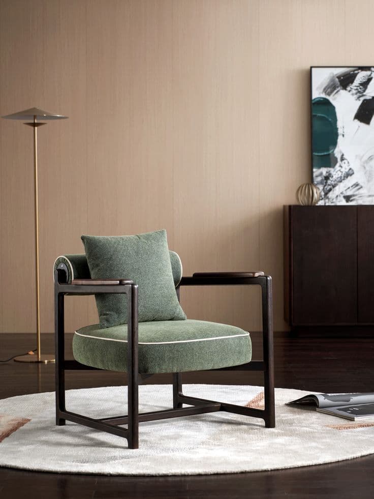 A modern lounge chair featuring a dark-stained exposed wood frame, upholstered in a green textured fabric. It includes a rounded seat cushion, a cylindrical bolster backrest, and a loose square back cushion, all with white contrast piping. The armrests are flat, topped with wooden caps. — 3D model