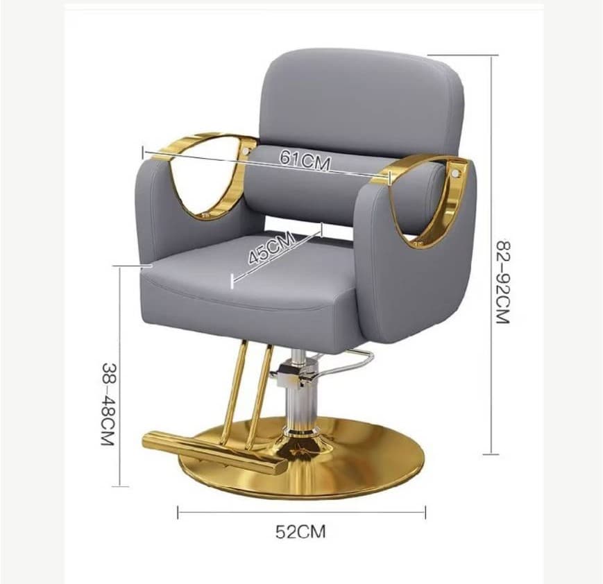 A modern salon or barber chair featuring light gray upholstered seating with prominent polished gold-tone metal accents. It includes a hydraulic base for height adjustment, a curved footrest, and open-loop armrests in gold. — 3D model