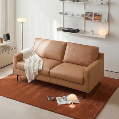 A modern two-seater sofa upholstered in tan leather, featuring clean lines, square armrests, and a low profile. It has two loose seat cushions and two loose back cushions, supported by slender, tapered black metal legs. A white throw blanket is draped over one armrest and cushion. — 3D model