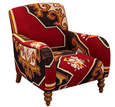 An upholstered armchair featuring a distinctive Kilim-style geometric pattern across its entire surface. The chair has a traditional club chair silhouette with rolled arms and a relatively compact form. It is supported by four wooden legs, with the front two being ornately turned and the rear two appearing more tapered and straight. The fabric displays a vibrant color palette of deep red, black, gold/ochre, and cream, with accents of orange and white, forming intricate interlocking motifs and borders. The upholstery covers all visible parts of the frame, including the back, seat, and arms, creating a cohesive and bold design statement. — 3D model