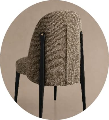 A contemporary dining chair with a rounded, upholstered back and seat. The upholstery has a textured, boucle-like finish. The chair features slender, dark-colored legs, likely made of wood or metal, with visible brass-toned fasteners connecting the seat frame to the legs. — 3D model