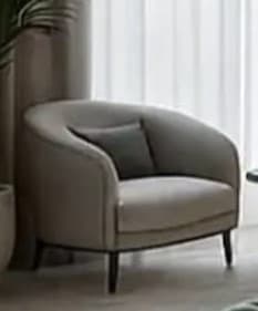 A contemporary upholstered armchair with a rounded barrel back, light beige fabric, dark piping detail, and tapered dark wood legs, accompanied by a small grey toss pillow. — 3D model