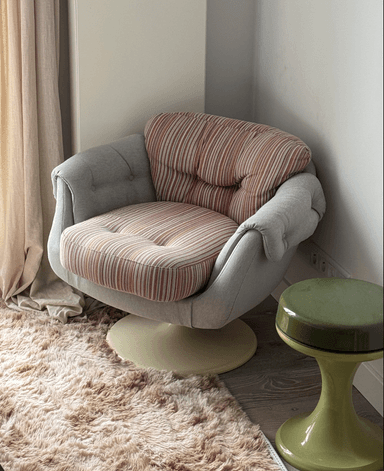A contemporary armchair with a rounded silhouette, featuring a tufted backrest and a plush seat cushion. The armchair is upholstered in two distinct fabrics: a textured, light gray fabric for the main body and a striped fabric with shades of brown and white for the seat and back cushions. It is supported by a rotating, cream-colored pedestal base. — 3D model