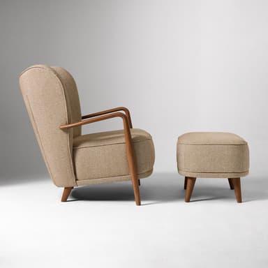A mid-century modern style armchair with a matching ottoman. The armchair features a high, winged backrest with button tufting and curved wooden armrests. The upholstery is a textured, light beige fabric. The ottoman is rectangular and upholstered in the same fabric, supported by four tapered wooden legs. — 3D model
