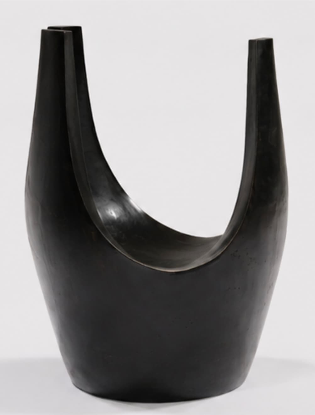 A dark, U-shaped sculptural stool, likely crafted from patinated bronze or ebonized wood. Its form is fluid and organic, with a deep, curved seat integrated into the continuous structure. The material exhibits a smooth, subtly reflective finish. — 3D model