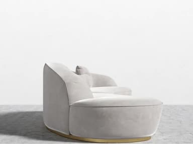 A contemporary curved modular sofa upholstered in light gray velvet, featuring an integrated backrest and armrests, supported by a recessed polished brass plinth base. It includes two matching throw pillows. — 3D model