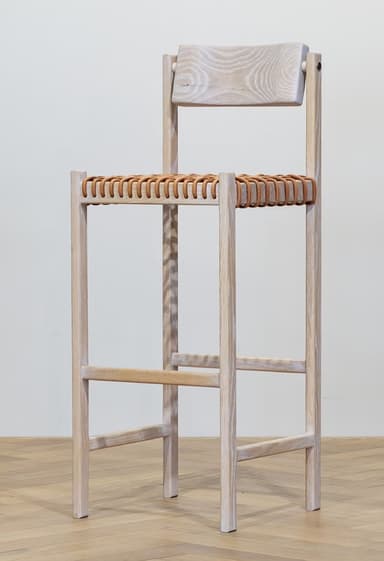 A tall bar stool with a light wood frame and a woven seat and backrest. The frame consists of four vertical legs connected by horizontal stretchers. The seat is made of intertwined leather straps, and the backrest is a solid, slightly curved wooden piece attached to the upper part of the frame. — 3D model