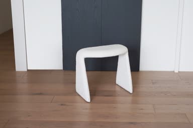 A white, textured stool with a unique U-shaped base. The stool appears to be upholstered in a boucle or teddy bear fabric. Its curved structure provides a modern and organic aesthetic. — 3D model
