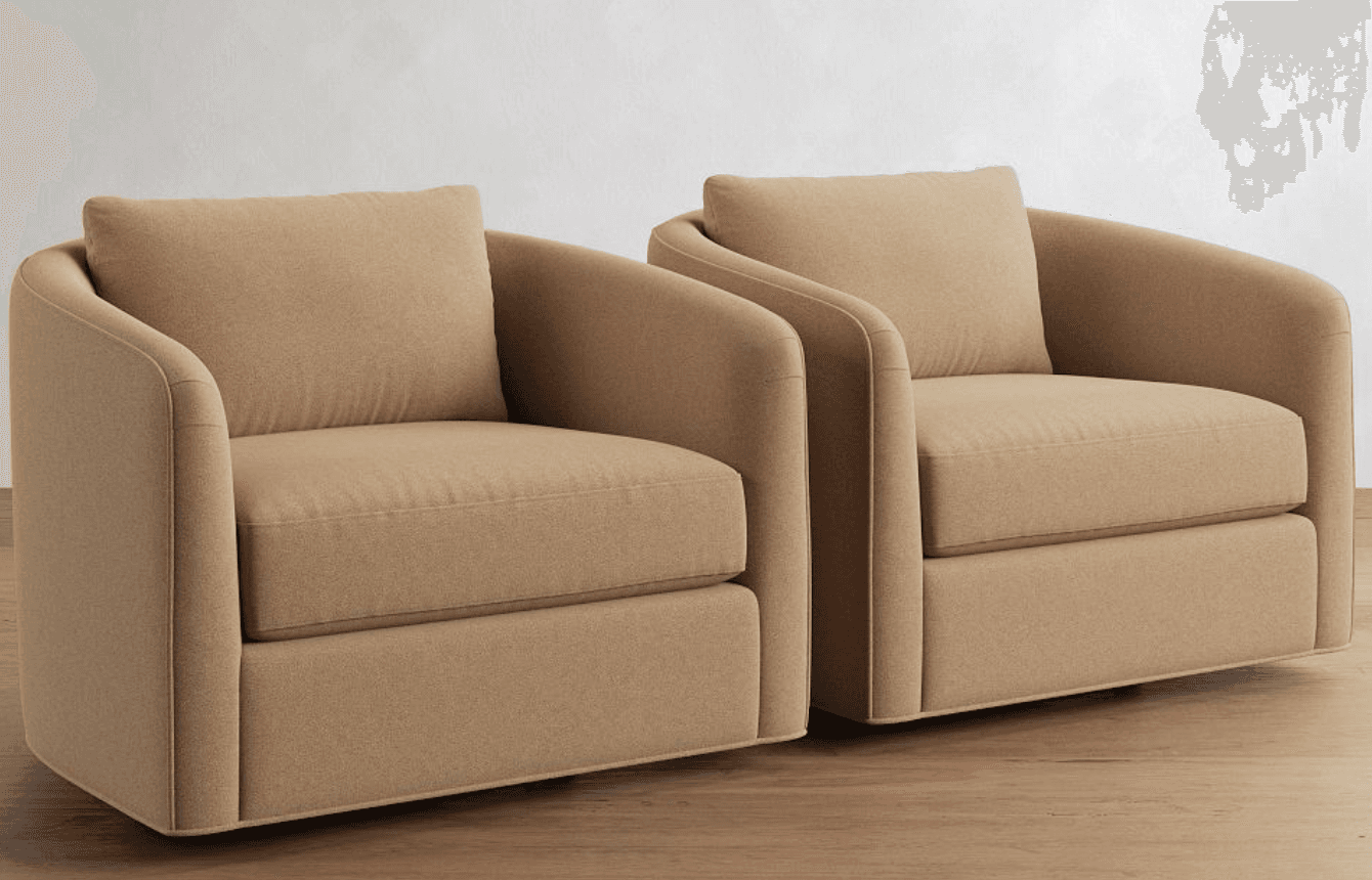 A pair of contemporary upholstered armchairs, each featuring a rounded silhouette with integrated arms and a fully upholstered skirted base. They are covered in a textured beige/tan fabric and include a loose seat cushion and a matching loose back cushion, contributing to a soft and inviting aesthetic. — 3D model