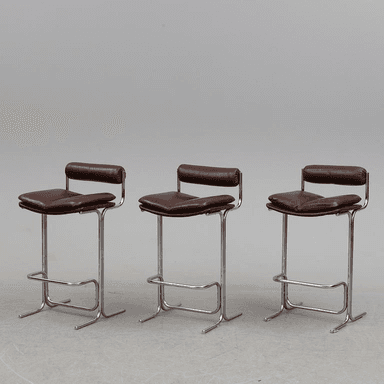 A modern bar stool featuring a gleaming tubular chrome frame and upholstered in rich brown leather. It has a padded square seat and a small, padded backrest for comfort, along with an integrated footrest. — 3D model