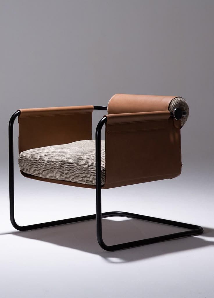 A modern armchair with a cantilever base, featuring a tubular black metal frame. The seat is upholstered in a textured light-colored fabric. The armrests are formed by brown leather straps that drape over the frame and extend to form side panels. A cylindrical headrest, also upholstered in brown leather, is attached to the top of the back frame. — 3D model