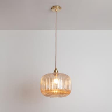 A single amber ribbed glass pendant light featuring brass hardware for mounting and suspension. The glass shade is a rounded rectangular form with vertical fluting, enclosing a visible light bulb. A fabric-covered electrical cord connects the shade to a circular brass canopy, providing a sleek and modern design with warm, diffused illumination. — 3D model
