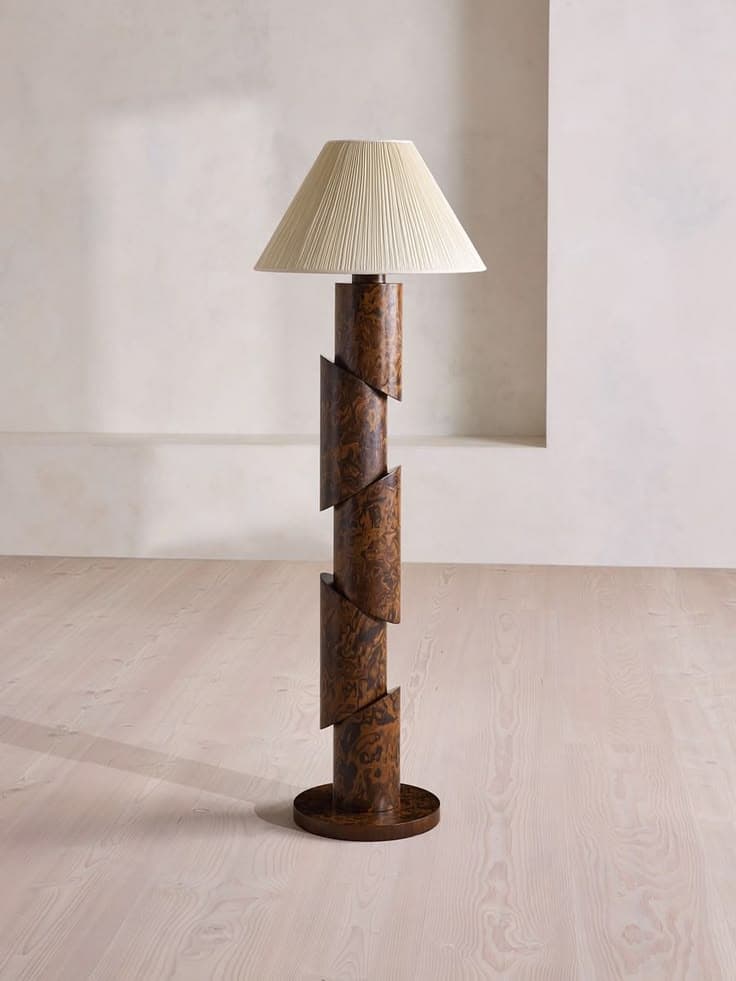 A tall floor lamp featuring a distinctive segmented and slightly spiraled stem made from burled wood or wood veneer, resting on a circular base. It is topped with a conical, pleated fabric lampshade in a light, neutral color. — 3D model