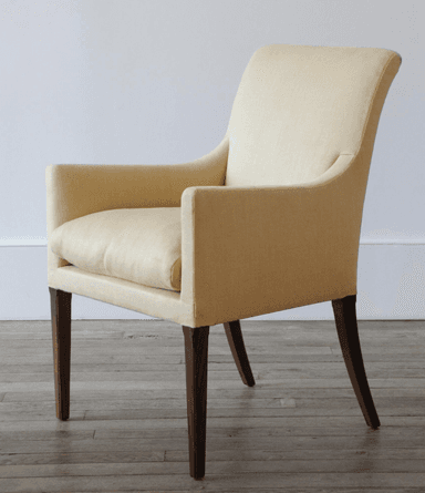 A fabric-upholstered armchair with a gently curved backrest and integrated armrests. The chair features four dark wooden legs, with the rear legs exhibiting a slight curve. The upholstery appears to be a textured woven fabric. — 3D model