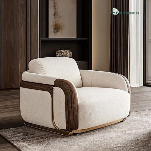 A contemporary upholstered armchair featuring a plush, rounded form. It showcases dark wood veneer accents along the outer armrests and back, complemented by subtle polished brass or gold-finished metal detailing near the base. The chair is upholstered in a light, textured cream or beige fabric, presenting a luxurious and inviting appearance. — 3D model