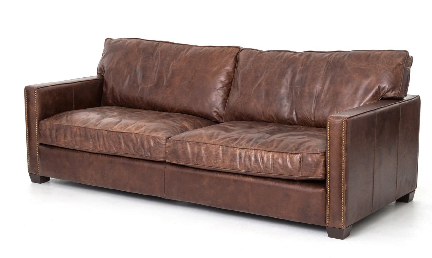 A two-seater sofa upholstered in distressed brown leather. It features a low profile with square arms and a tailored skirt. The arms and base are adorned with decorative brass nailhead trim. The cushions appear overstuffed and provide a relaxed, comfortable aesthetic. — 3D model