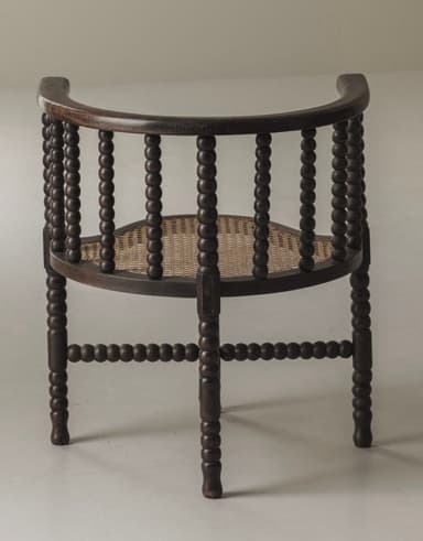 A dark stained wooden barrel armchair featuring a bobbin-turned frame and a woven cane seat. The back and armrests form a continuous curved structure, supported by vertical bobbin-turned spindles. The four bobbin-turned legs are connected by bobbin-turned stretchers forming an X-shape beneath the seat. The seat itself is crafted from woven cane with a slightly curved front. — 3D model