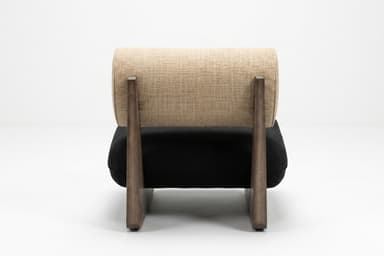 A modern, low-profile lounge chair featuring a distinctive solid wood base. The base is dark-toned wood, shaped with a geometric, wedge-like profile. It supports a plush, rectangular black seat cushion, likely upholstered in velvet or microsuede. The backrest is a cylindrical bolster cushion, upholstered in a textured light beige fabric, resting against the angled wooden support structure. — 3D model