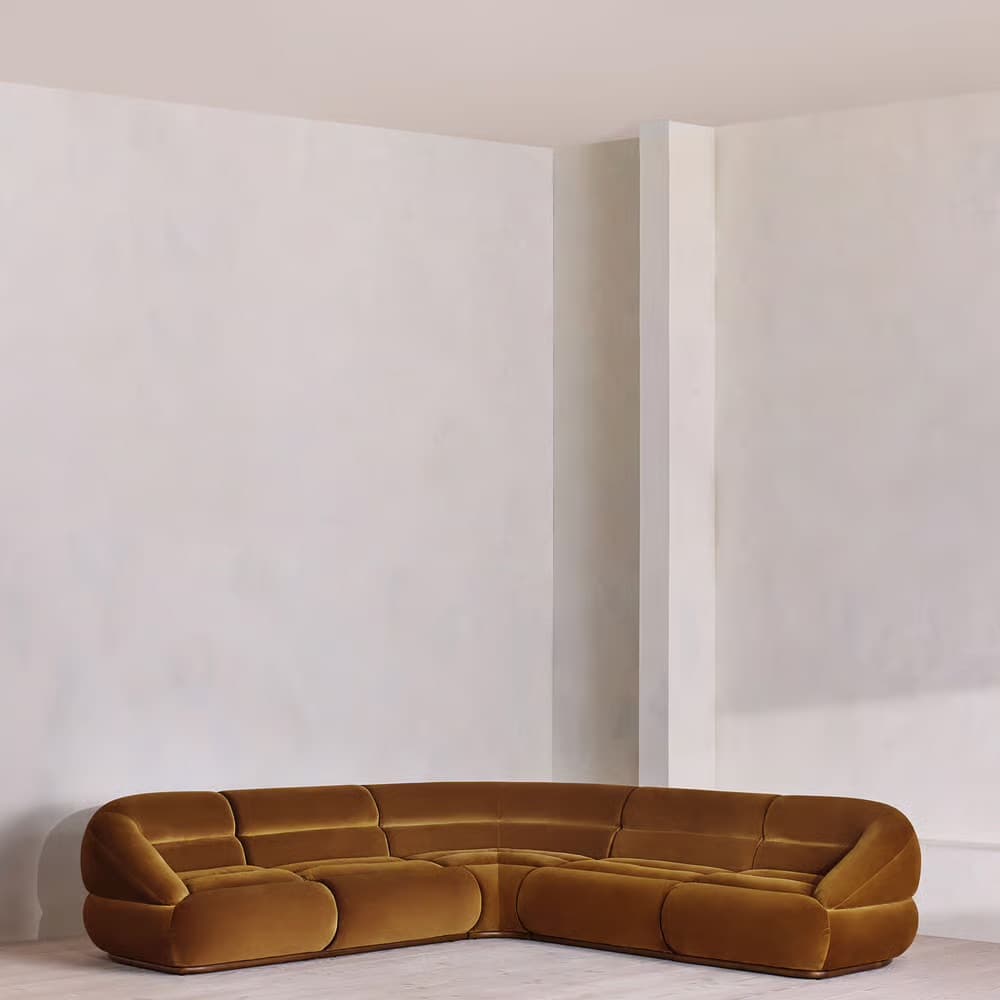 A modular sectional sofa with rounded edges and a plush velvet upholstery. The sofa is configured in a corner arrangement, featuring deep seats and back cushions with horizontal tufting. The design is low-profile and appears to be upholstered in a warm, mustard-yellow or ochre velvet fabric. — 3D model