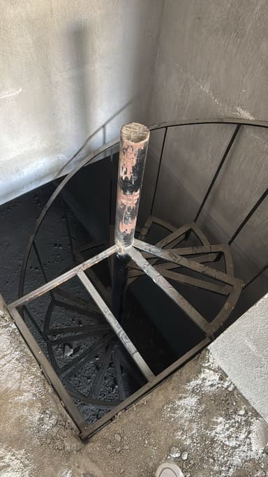 A spiral staircase constructed from metal. It features a central vertical pole supporting a series of wedge-shaped steps that spiral upwards. Vertical railings along the outer edge provide support and safety. The metal shows signs of rust and weathering. — 3D model