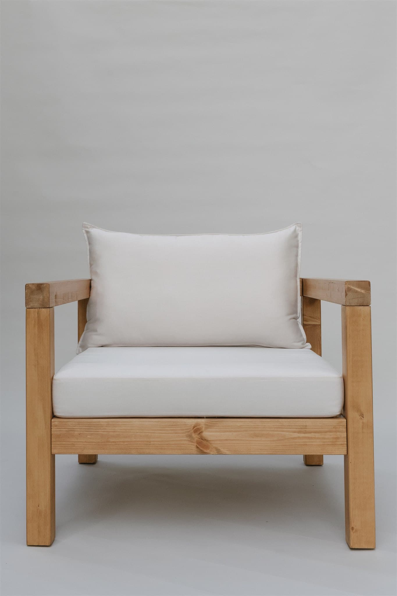 A single armchair with a solid wood frame and upholstered cushions. The frame consists of thick, square-profile wooden beams for the legs, base, and arms. The seat and back are padded with white cushions. A rectangular lumbar pillow is placed against the back cushion. — 3D model