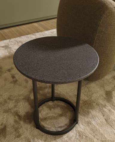 A small, round accent table featuring a dark, granular-textured top and a minimalist metal base with three slender legs connected by a circular stretcher. — 3D model