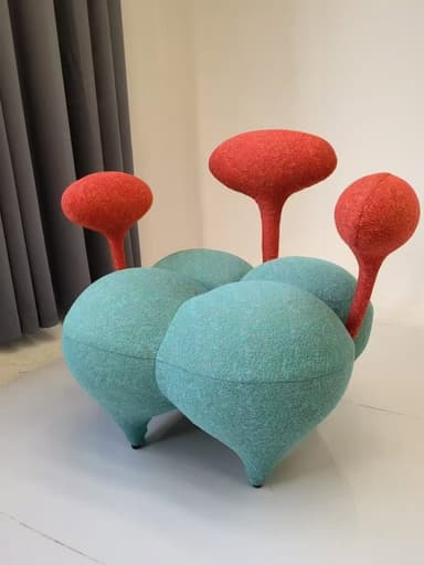 A whimsical and modern sculptural seating unit, featuring four organically shaped, rounded teal textile cushions forming the base. From these cushions, three upright, mushroom-like forms with textured orange textile rise, serving as backrests or decorative elements. The piece exhibits an abstract, playful design aesthetic. — 3D model