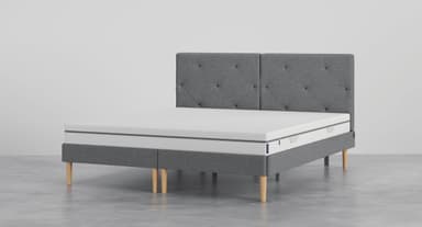 A modern platform bed featuring a gray fabric upholstered frame and a tufted headboard. The bed is supported by light-colored, tapered wooden legs, and includes a white mattress. — 3D model