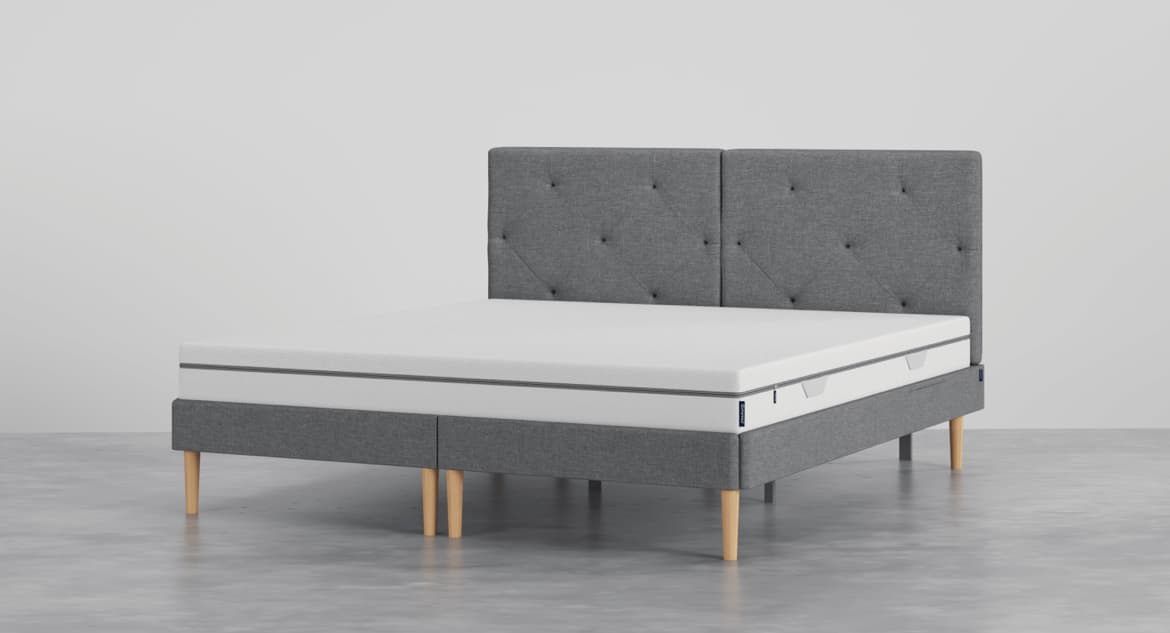A modern platform bed featuring a gray fabric upholstered frame and a tufted headboard. The bed is supported by light-colored, tapered wooden legs, and includes a white mattress. — 3D model