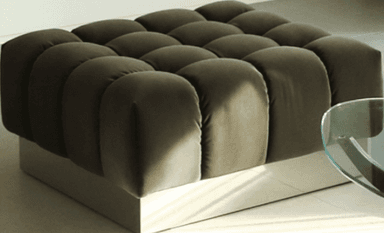 A dark brown, square, upholstered ottoman featuring a distinctive modular bubble tufting pattern on its top and sides, resting on a flat, low-profile light grey plinth base. — 3D model