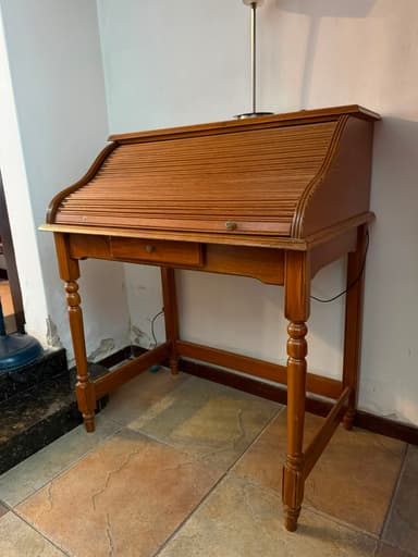 A traditional wooden roll-top secretary desk featuring a slatted roll-top mechanism that conceals the work surface. The desk includes a single central drawer below the roll-top section, equipped with a small wooden knob. It stands on four turned legs, connected by stretchers on the sides and front, suggesting a classic or antique aesthetic. The desk is finished in a medium brown wood tone. — 3D model