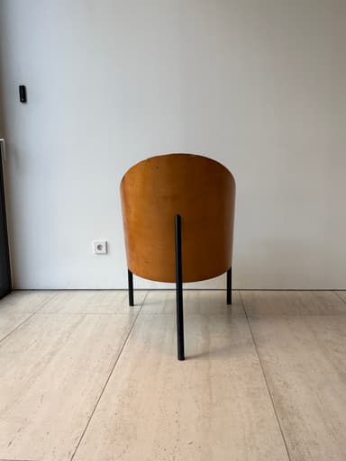 A striking mid-century modern lounge chair featuring a gracefully curved, light-brown plywood shell that forms both the backrest and integrated armrests. The chair is supported by a minimalist black metal frame with slender legs. A dark, possibly black or dark brown, upholstered cushion rests on the seat, contrasting with the warm wood tones. — 3D model