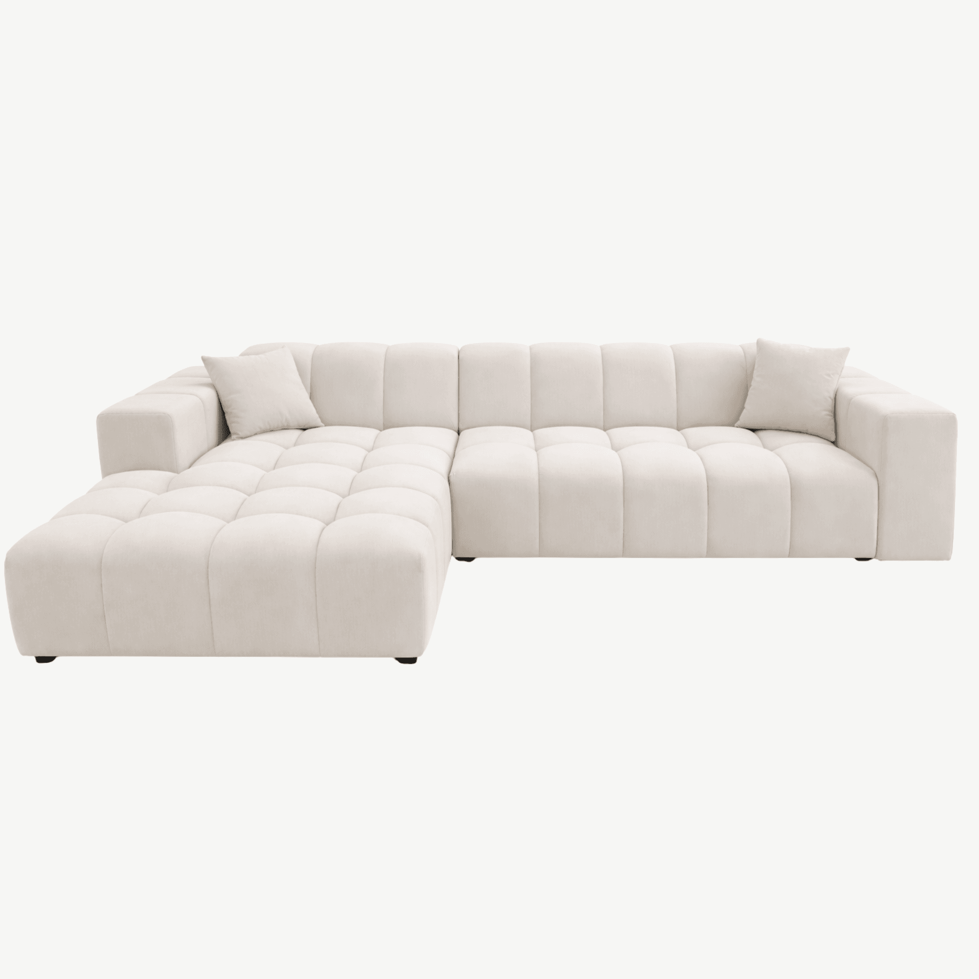 A contemporary sectional sofa with a tufted upholstery design. The sofa features a chaise lounge section extending from the main body. It is upholstered in a light cream-colored fabric with a soft texture. The design incorporates horizontal tufting on the seat and back cushions, creating a grid-like pattern. Two square throw pillows, matching the sofa's upholstery, are placed on the sofa. The sofa sits on low-profile, dark-colored feet. — 3D model
