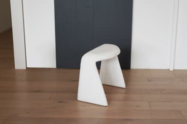 A white, textured stool with a unique U-shaped base. The stool appears to be upholstered in a boucle or teddy bear fabric. Its curved structure provides a modern and organic aesthetic. — 3D model