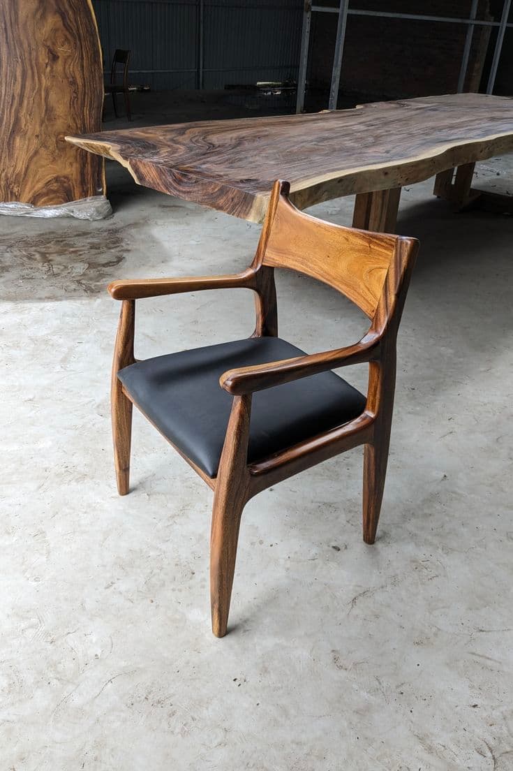 A Mid-Century Modern style dining armchair crafted from rich, dark wood with a distinct grain, featuring a contoured, integrated backrest and armrests, and an upholstered black leather seat. The chair's design emphasizes organic curves and sculpted lines. — 3D model
