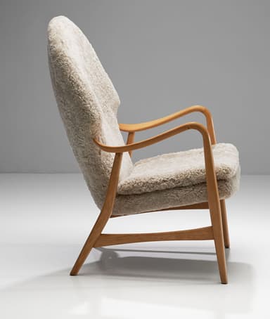 A high-backed armchair with a wooden frame and plush sheepskin upholstery. The frame consists of curved wooden arms and legs. The seat and back are fully upholstered in a textured, cream-colored sheepskin material, giving it a soft and inviting appearance. The design suggests a focus on comfort and organic forms. — 3D model