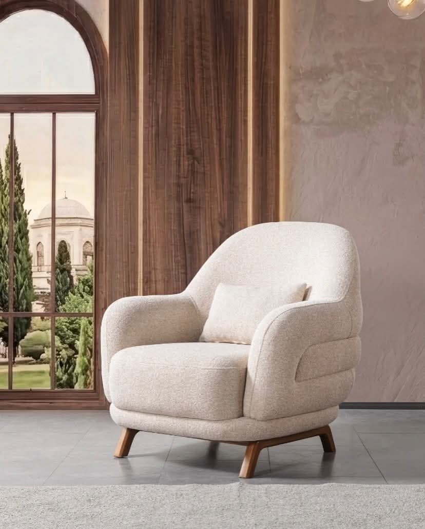 A contemporary upholstered armchair with a light-colored bouclé fabric, featuring rounded armrests, a cushioned seat, and four splayed wooden legs. It includes a small rectangular lumbar pillow. — 3D model