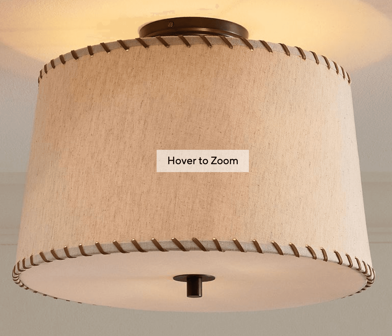 A semi-flush mount ceiling light featuring a cylindrical drum shade crafted from light beige or cream-colored fabric. The top and bottom edges of the drum shade are adorned with a decorative lacing detail, resembling stitching in a darker brown or bronze hue. The light is mounted to the ceiling by a dark bronze or oil-rubbed bronze circular canopy, and a matching finial is visible at the center of the bottom diffuser, securing it in place. The fabric shade provides diffused light. — 3D model