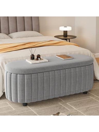 An oval-shaped upholstered bench in light grey fabric, featuring vertical channel tufting along its sides and supported by small, discreet black feet. — 3D model