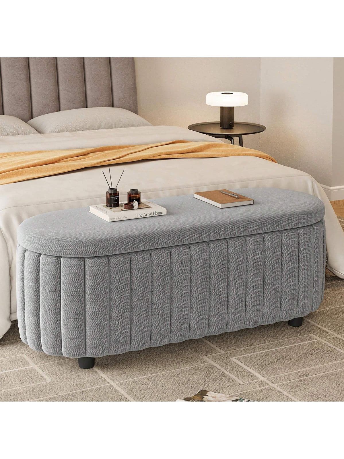 An oval-shaped upholstered bench in light grey fabric, featuring vertical channel tufting along its sides and supported by small, discreet black feet. — 3D model