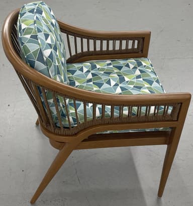 A barrel-back armchair featuring a warm-toned wooden frame, likely teak or oak, with distinctive woven or rope detailing along the arms and backrest. The chair is upholstered with removable seat and back cushions in a textured, multi-tonal green, white, and blue striped fabric. Its design combines elegant curves with a relaxed, tropical-modern aesthetic. — 3D model