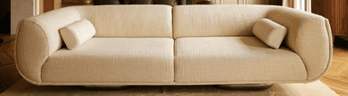 A modern, two-seater sofa with rounded edges and a low profile. The sofa features a single seat cushion divided into two sections, and a removable cylindrical bolster pillow. The upholstery appears to be a textured fabric. — 3D model