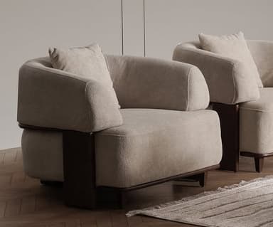 A contemporary upholstered armchair featuring a low-profile design, rounded forms, and distinct dark wood accents. The main body is covered in a light beige or cream textured fabric, and a matching square throw pillow is included. Dark wood elements form a structural and decorative band around the base and extend upwards on the sides, functioning as part of the armrests. The chair is supported by short, tapered dark wood legs. — 3D model