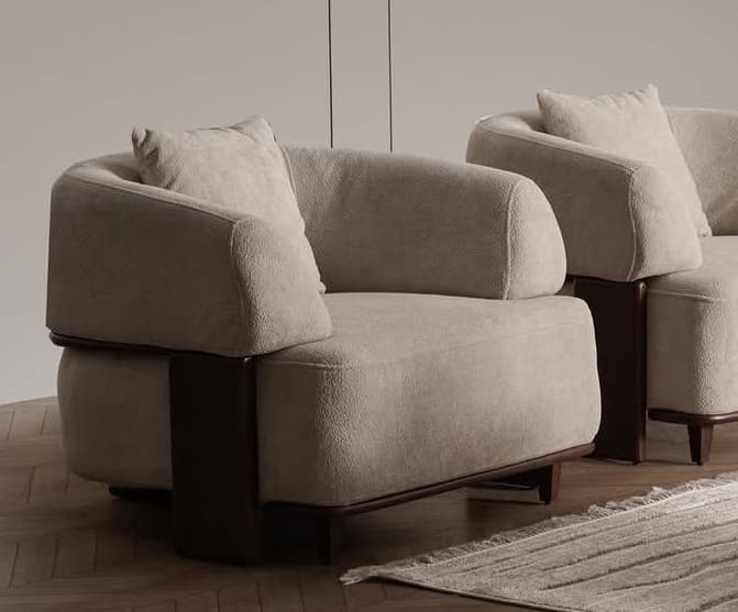 A contemporary upholstered armchair featuring a low-profile design, rounded forms, and distinct dark wood accents. The main body is covered in a light beige or cream textured fabric, and a matching square throw pillow is included. Dark wood elements form a structural and decorative band around the base and extend upwards on the sides, functioning as part of the armrests. The chair is supported by short, tapered dark wood legs. — 3D model