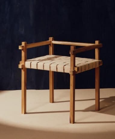 A minimalist, low-profile armchair constructed from light-colored wood featuring a woven strap seat and partial backrest/armrests. — 3D model