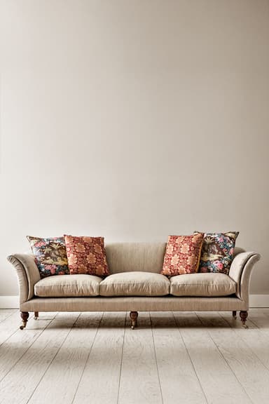 A traditional three-seater sofa upholstered in a neutral beige fabric, featuring classic rolled arms and dark turned wooden legs with brass casters. The sofa includes three separate seat cushions and several loose, patterned throw pillows. — 3D model