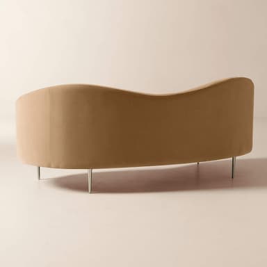 A modern curved back sofa upholstered in plush, champagne-colored velvet, featuring slender, polished stainless steel legs with a champagne finish. — 3D model