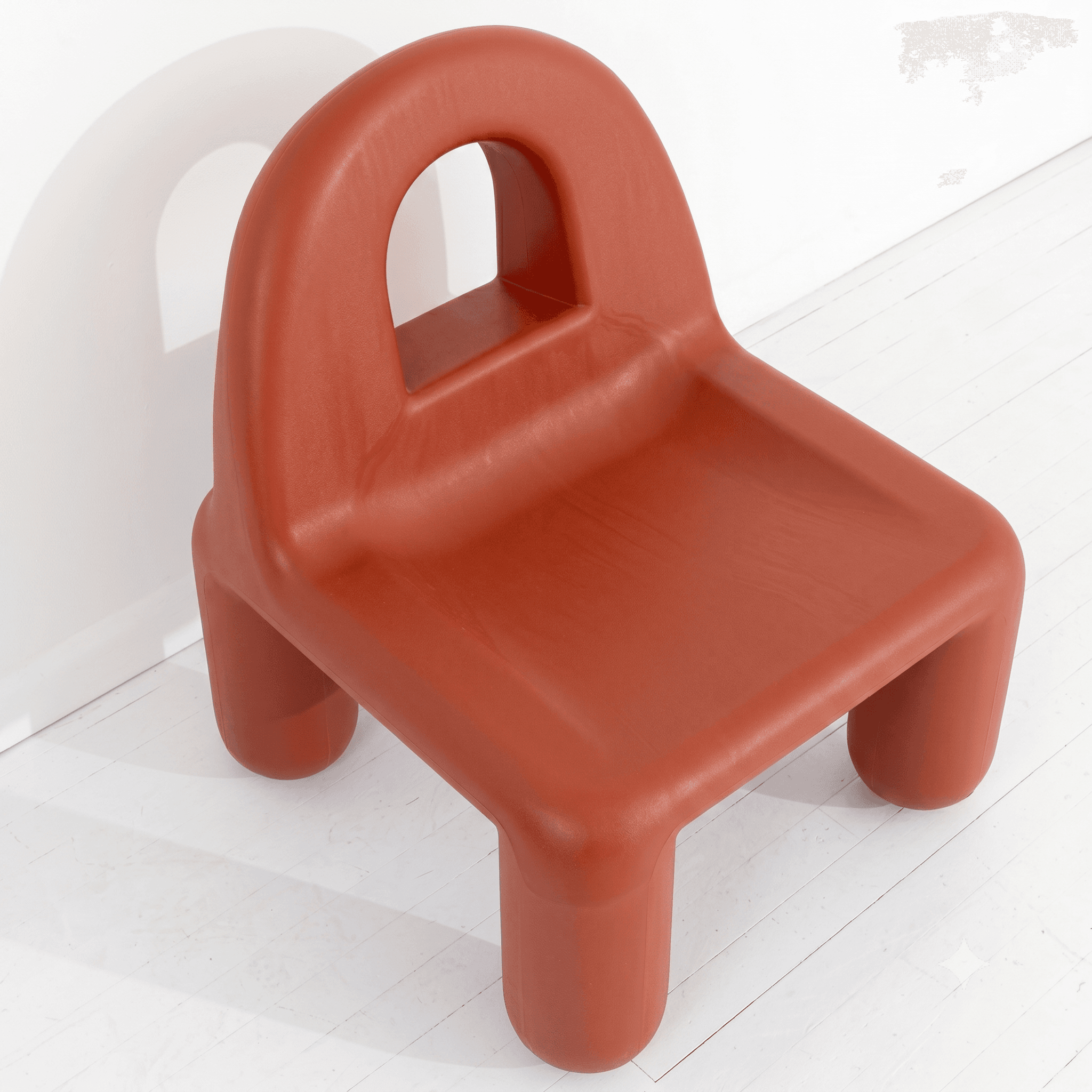 A small, unibody molded plastic children's chair rendered in a terracotta orange color. It features a wide, flat seat and a low, curved backrest that incorporates a semi-circular handle for easy portability. The chair is supported by four short, stout, cylindrical legs, all formed from the same continuous plastic material. — 3D model