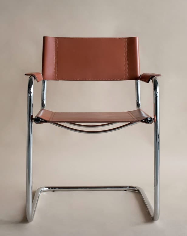 A modern armchair with a tubular chrome frame and leather upholstery. The seat and backrest are made of brown leather straps, and the armrests are also upholstered in leather. The frame is constructed from bent tubular metal, forming legs that extend upwards to support the seat and back. — 3D model