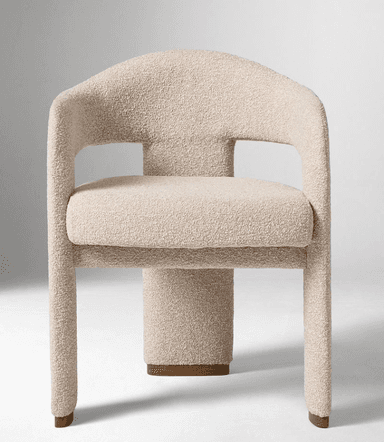 A modern armchair with a rounded backrest and armrests, upholstered in a textured boucle fabric. The chair features a substantial, cylindrical pedestal base with a subtle wood accent at the bottom, and two thick, curved legs extending from the sides of the seat. The overall design is sculptural and contemporary. — 3D model